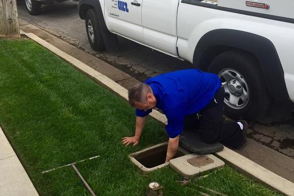 Man kneeling down to reach into a water service access point near the curb